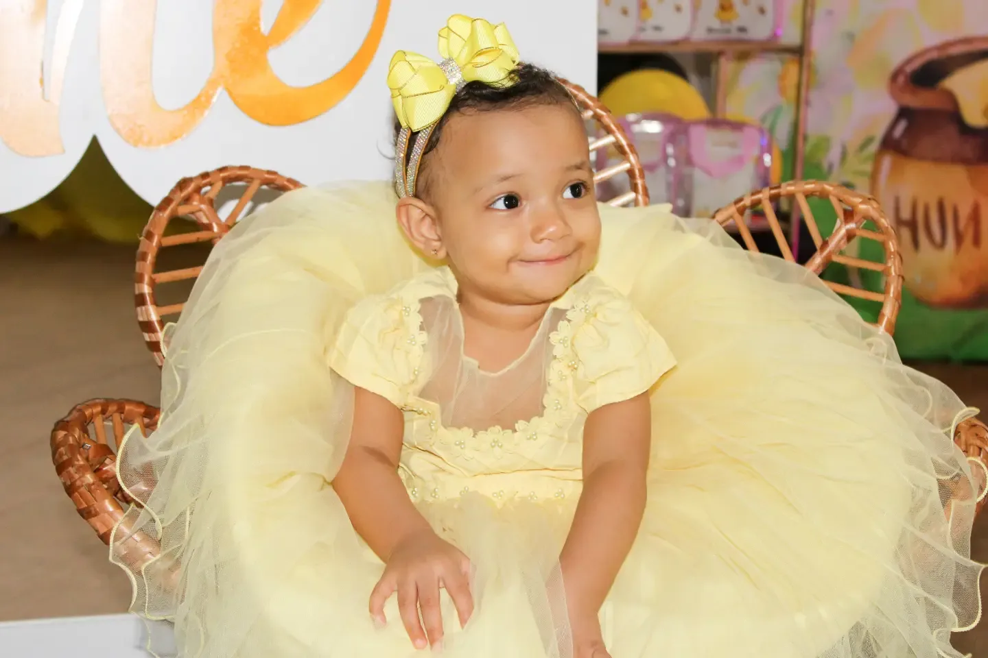 Bebê de vestido amarelo de tule sentada em uma poltrona, em festa de aniversário.