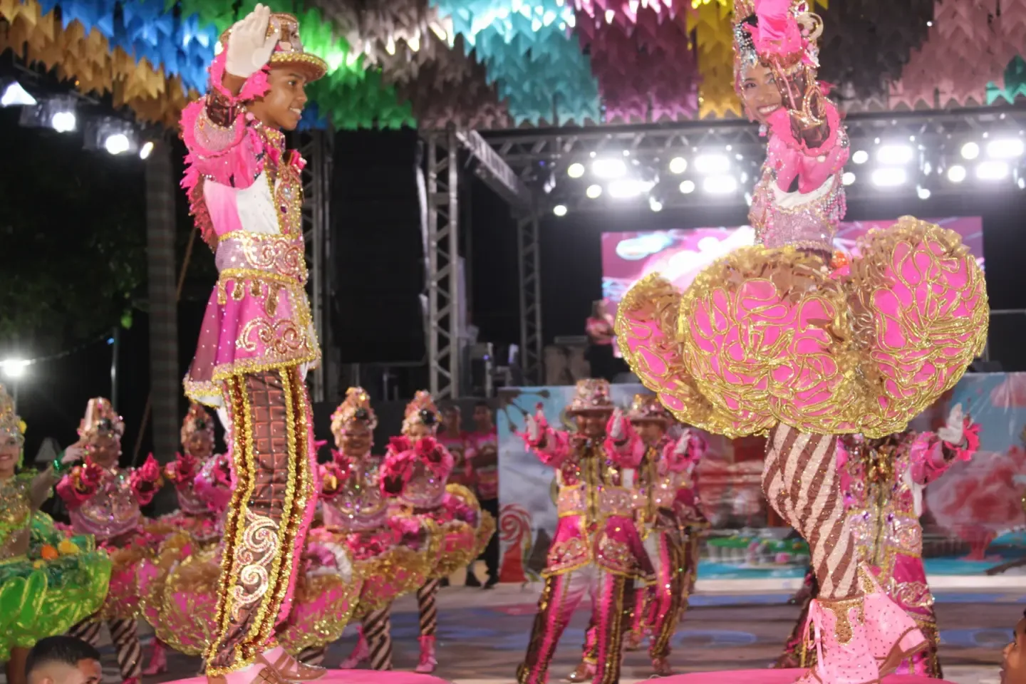 Dançarinos de figurino rosa se apresentam diante do palco iluminado.