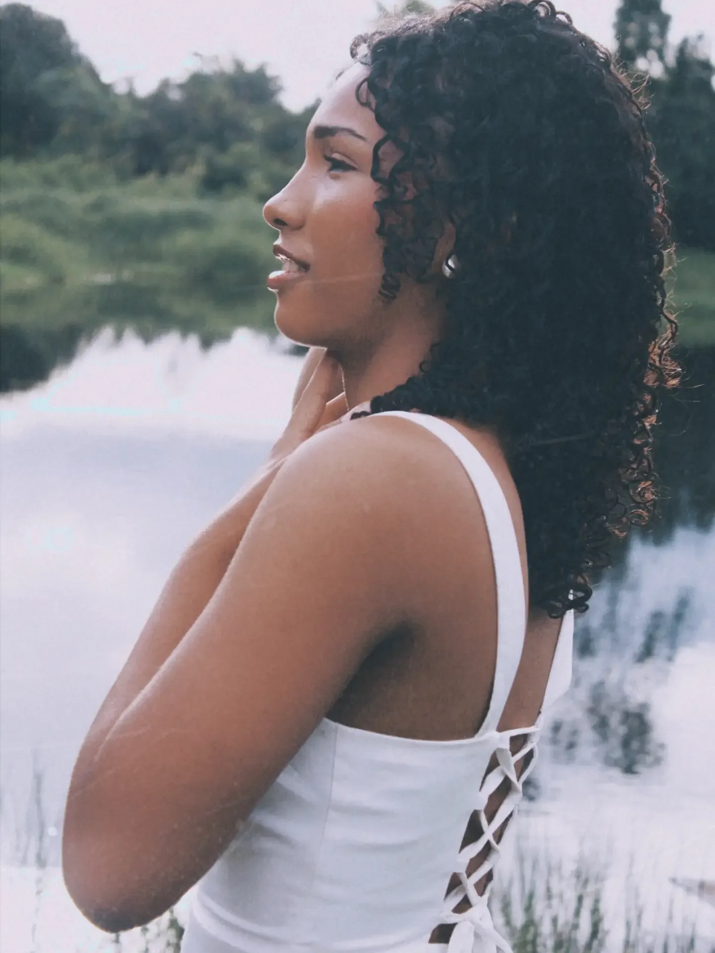 Perfil de mulher de cabelo cacheado e vestido branco diante de um lago.