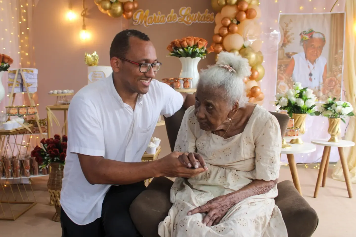 Homem segura as mãos de uma senhora sentada durante a festa.