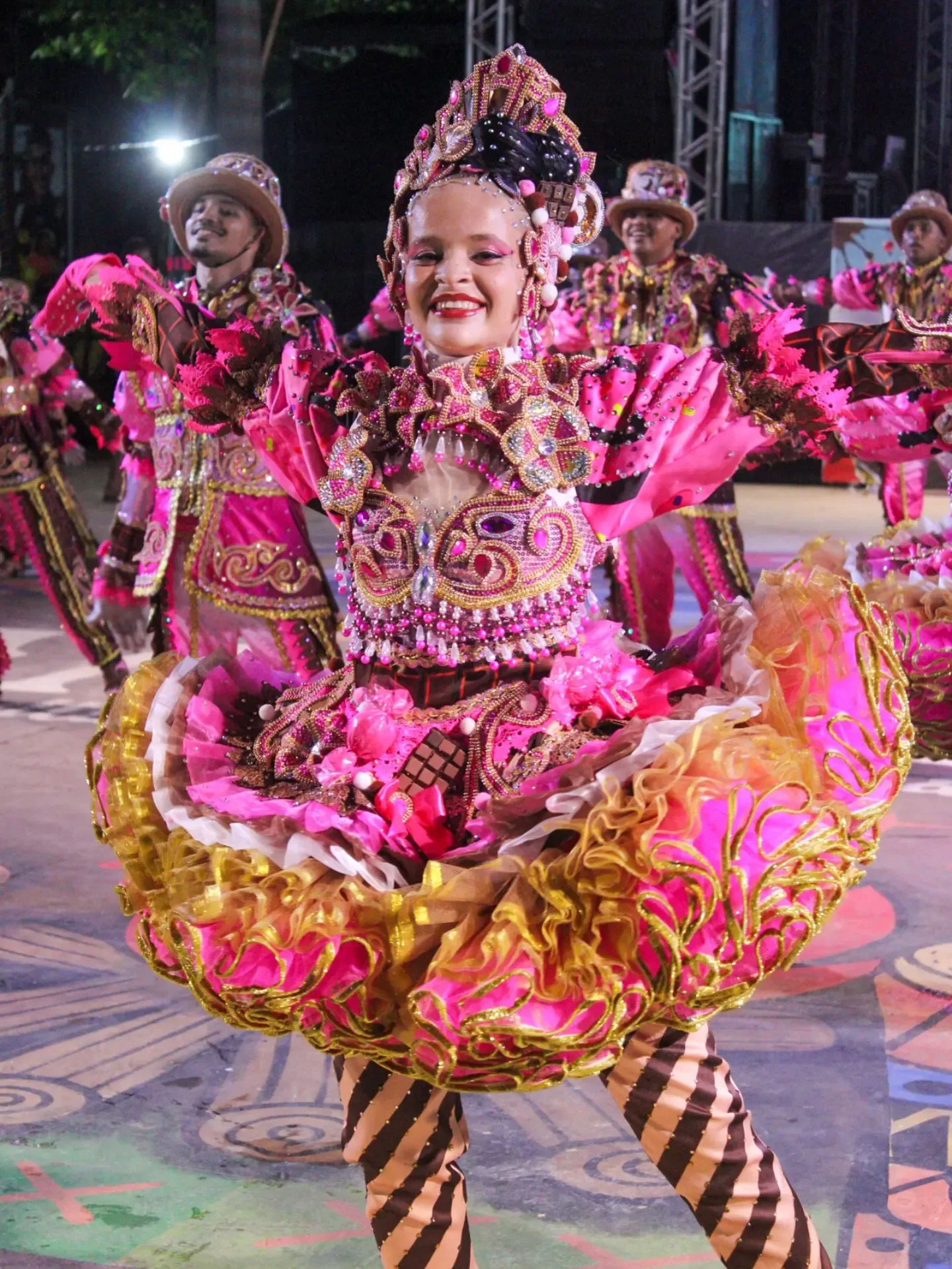 Dançarina com saia rodada rosa e dourada gira durante apresentação noturna.
